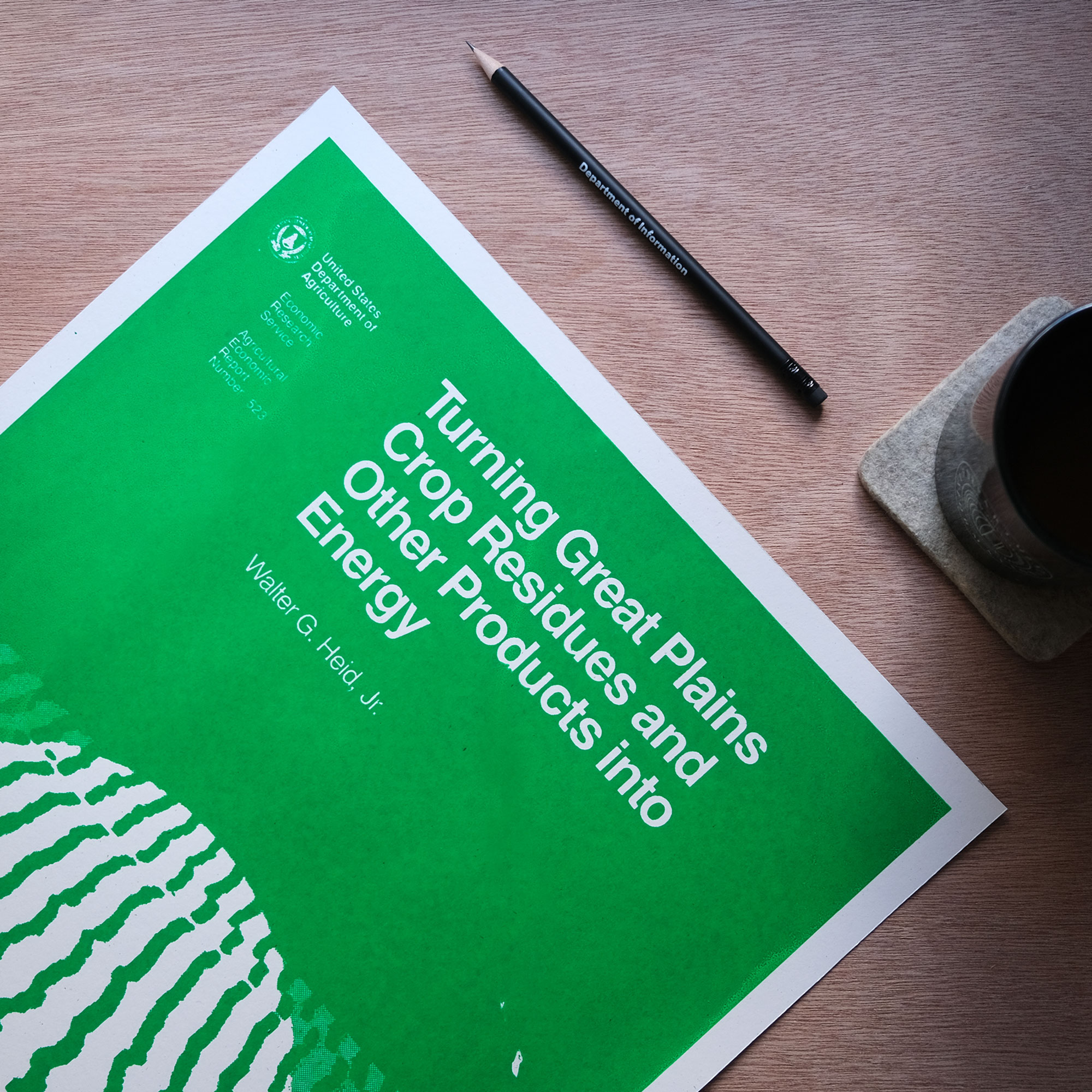 A bright green and white poster of the 1984 usda report cover for Turning Great Plains Crop Residues and Other Products into Energy sits on top of a wood surface