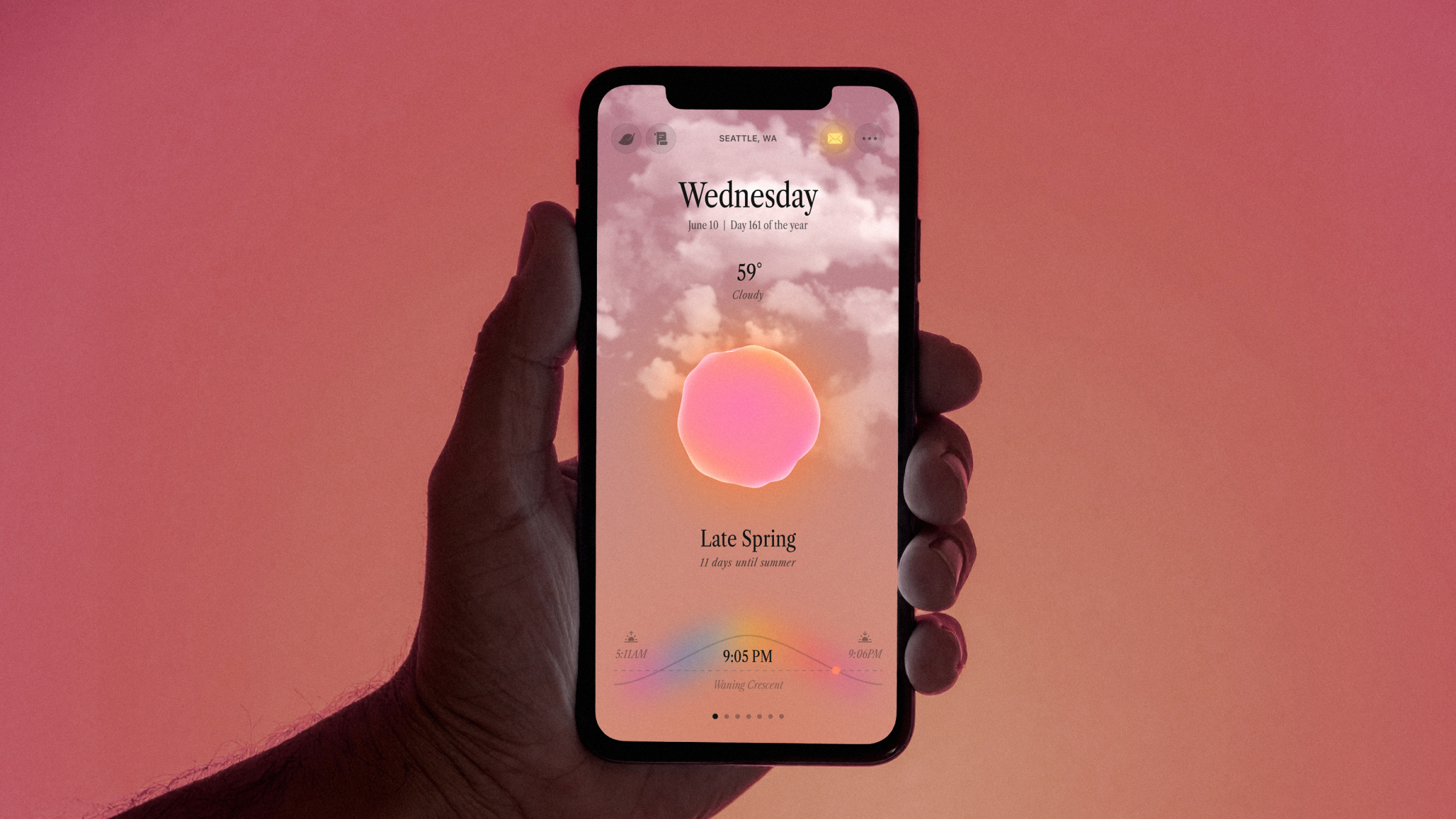 A hand hold a mobile phone in a pink room, the app Ambient Almanac is on the screen, pink sky with clouds, a pink glowing orb in the center, and lots of information about the day and weather around it