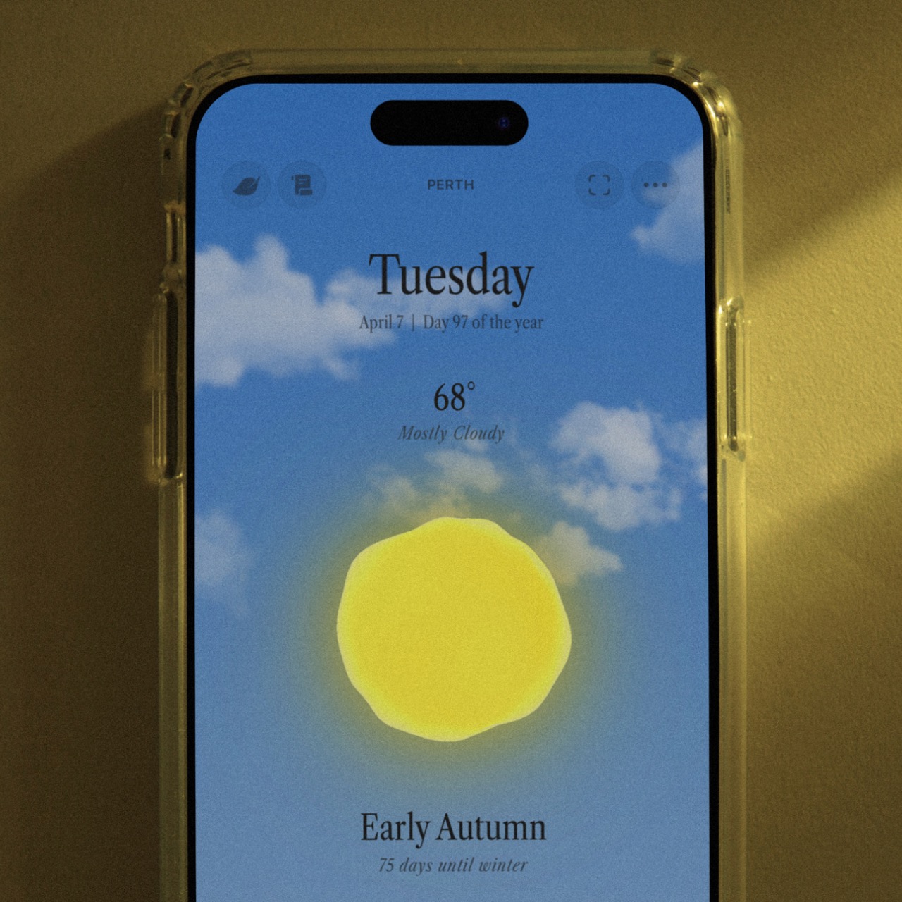 A close up view of the app Ambient Almanac shows a daytime scene with a yellow orb and blue sky and clouds