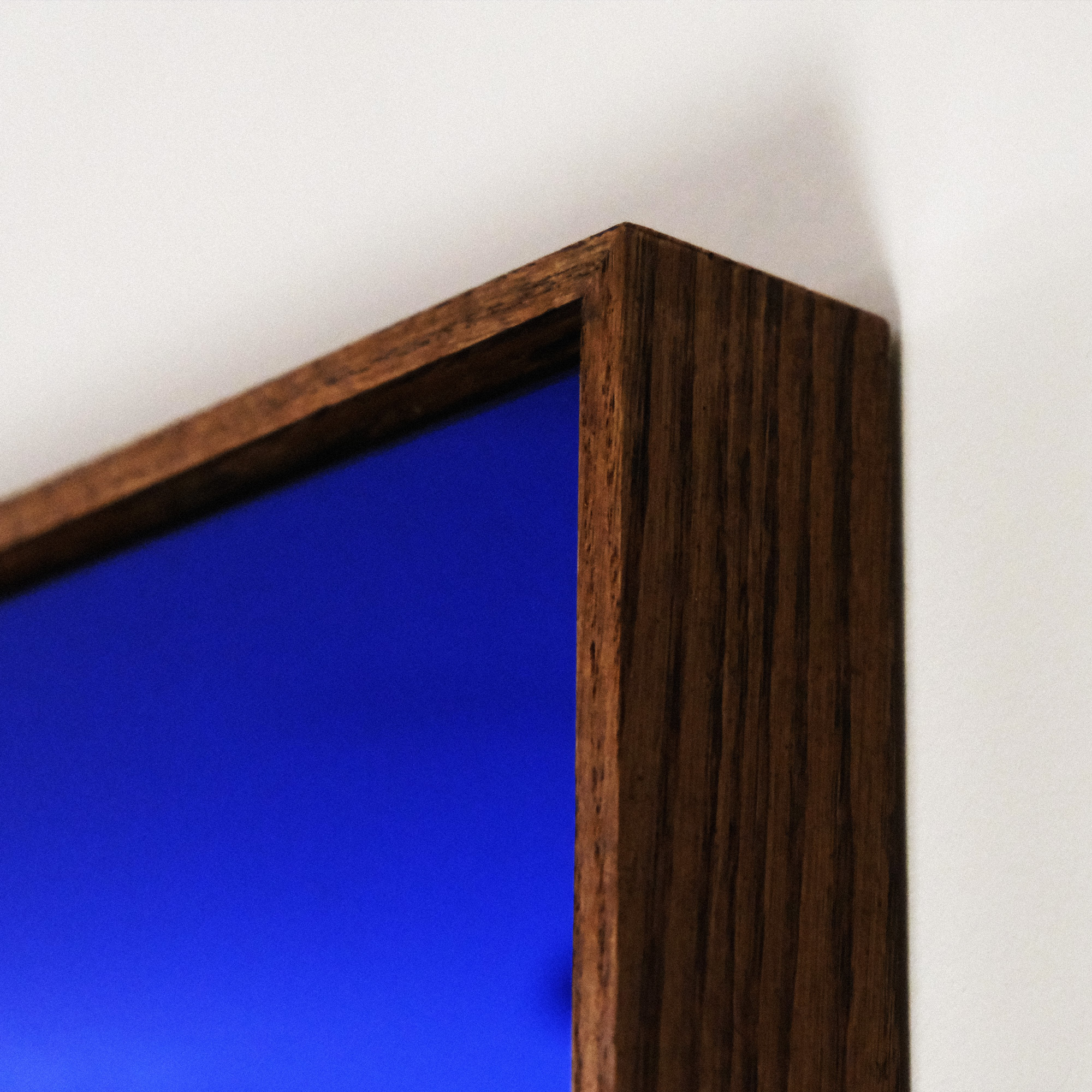 A close up of a dark oak frame corner holding a blue reflective mirror