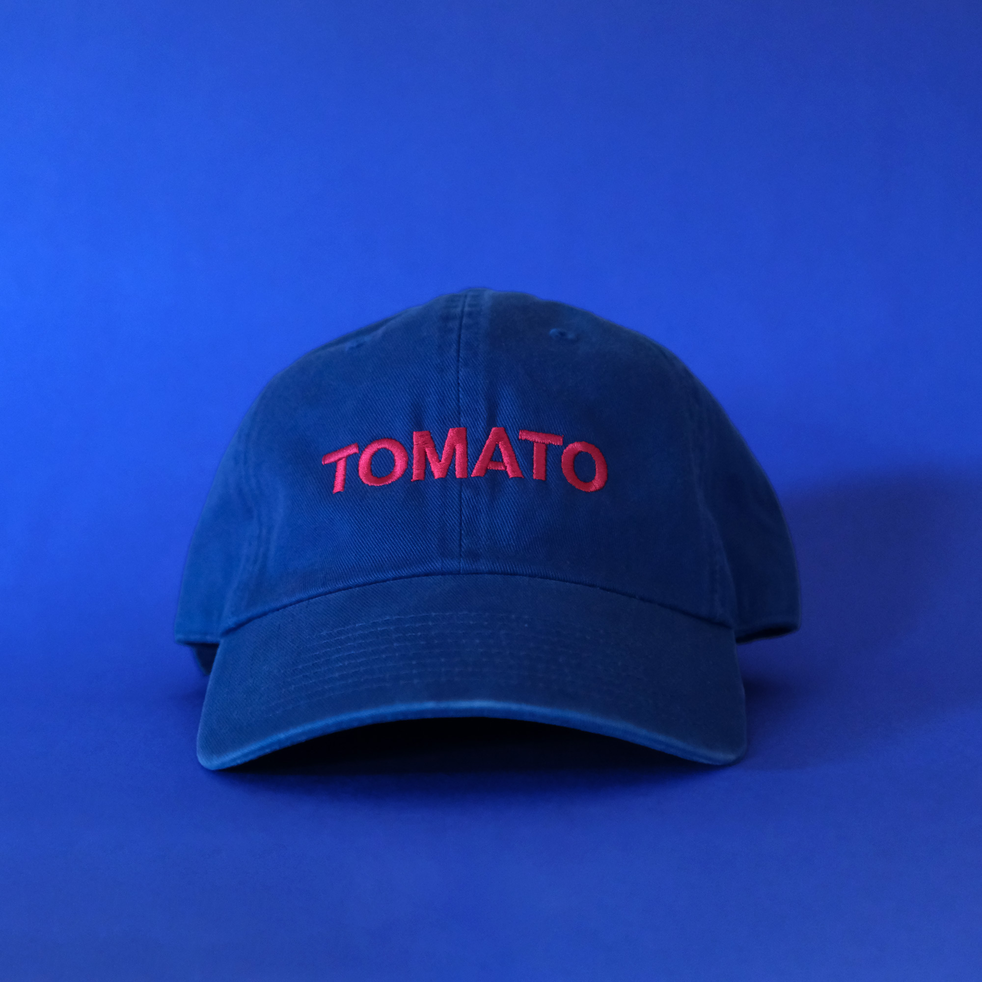 A bright blue cap with red embroidered text that says TOMATO on a blue background