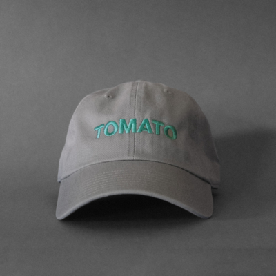 A light gray cap with seafoam embroidered text that says TOMATO