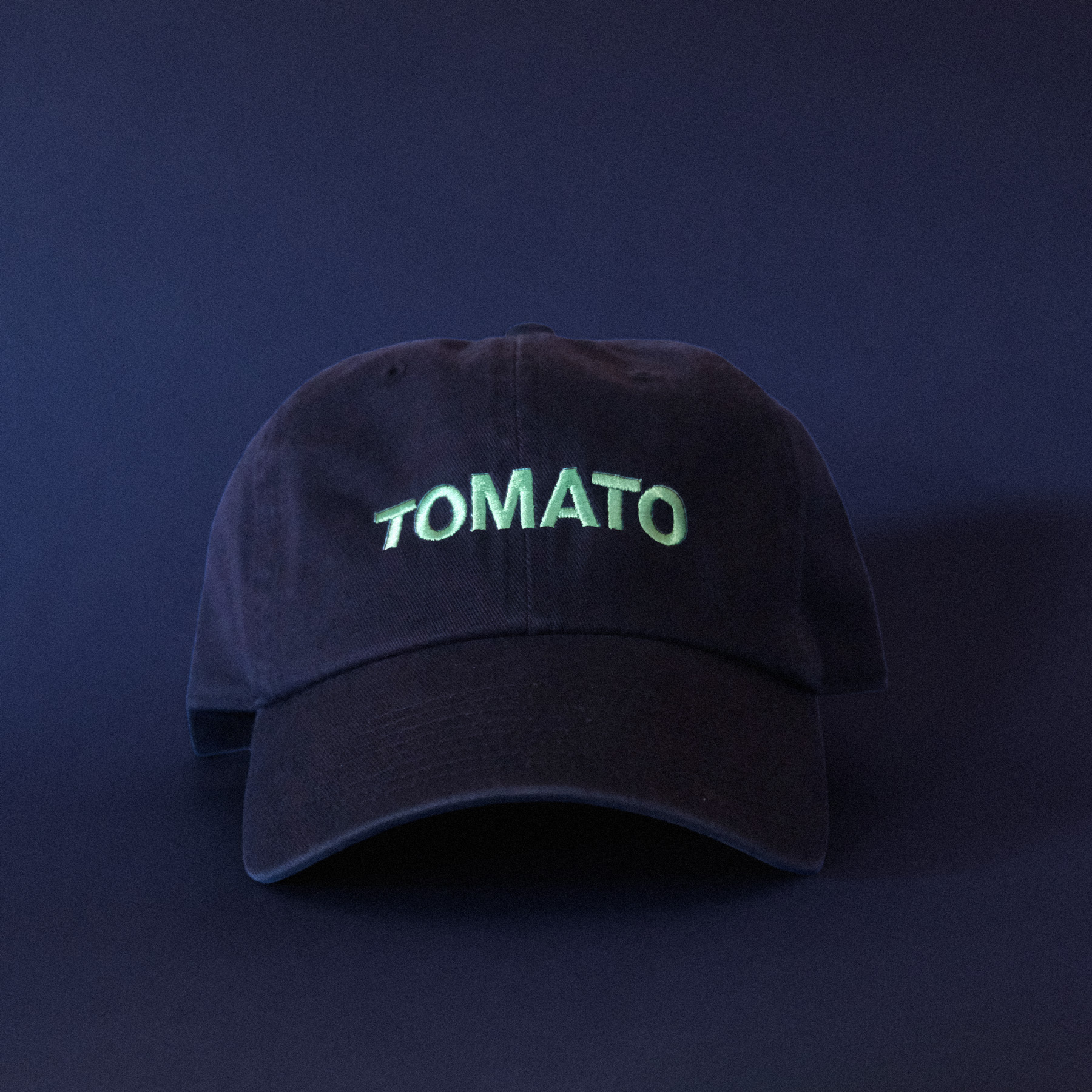 A dark blue cap with mint embroidered text that says TOMATO on a dark blue background